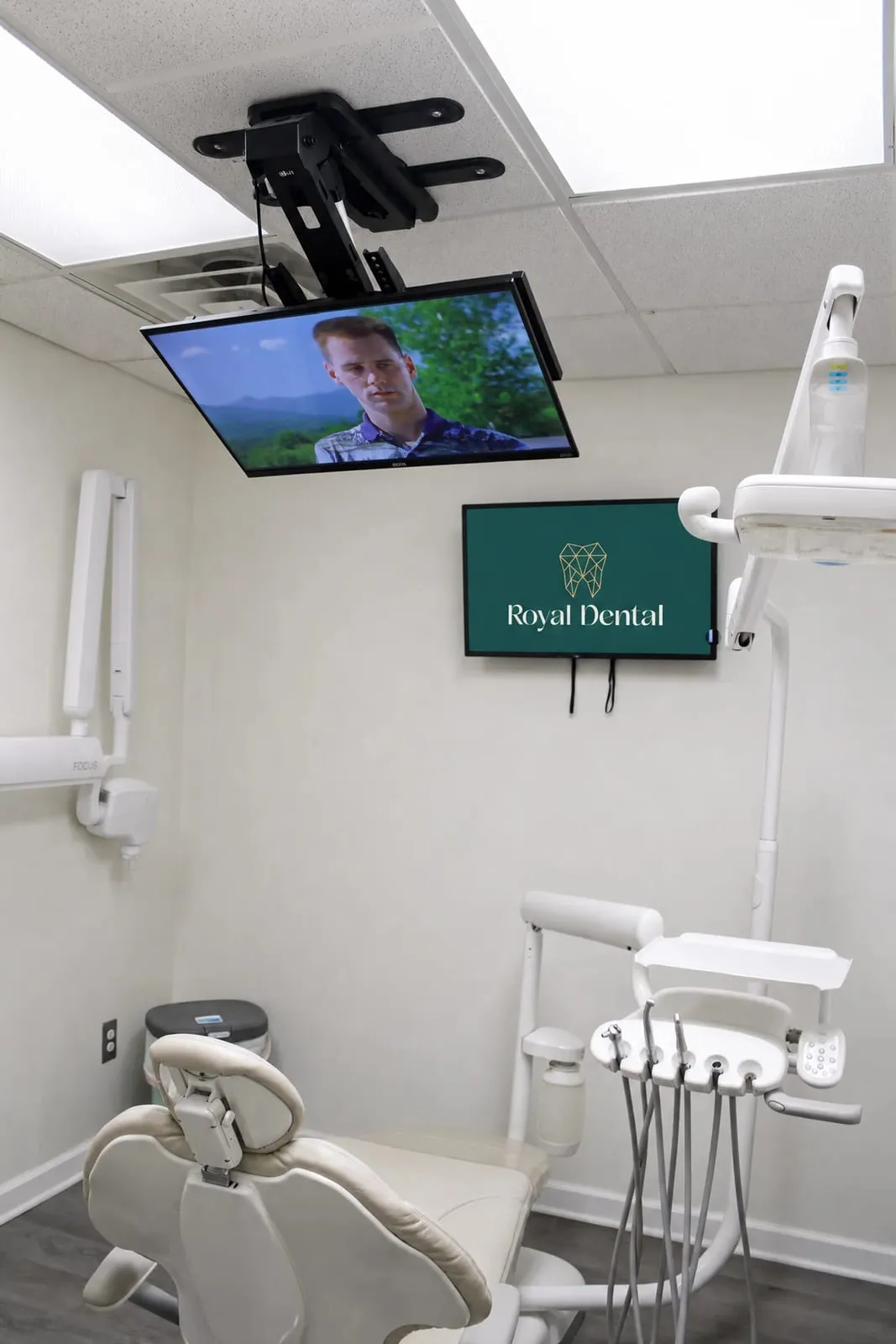 A Royal Dental Center treatment room with a ceiling mounted TV above the dental chair
