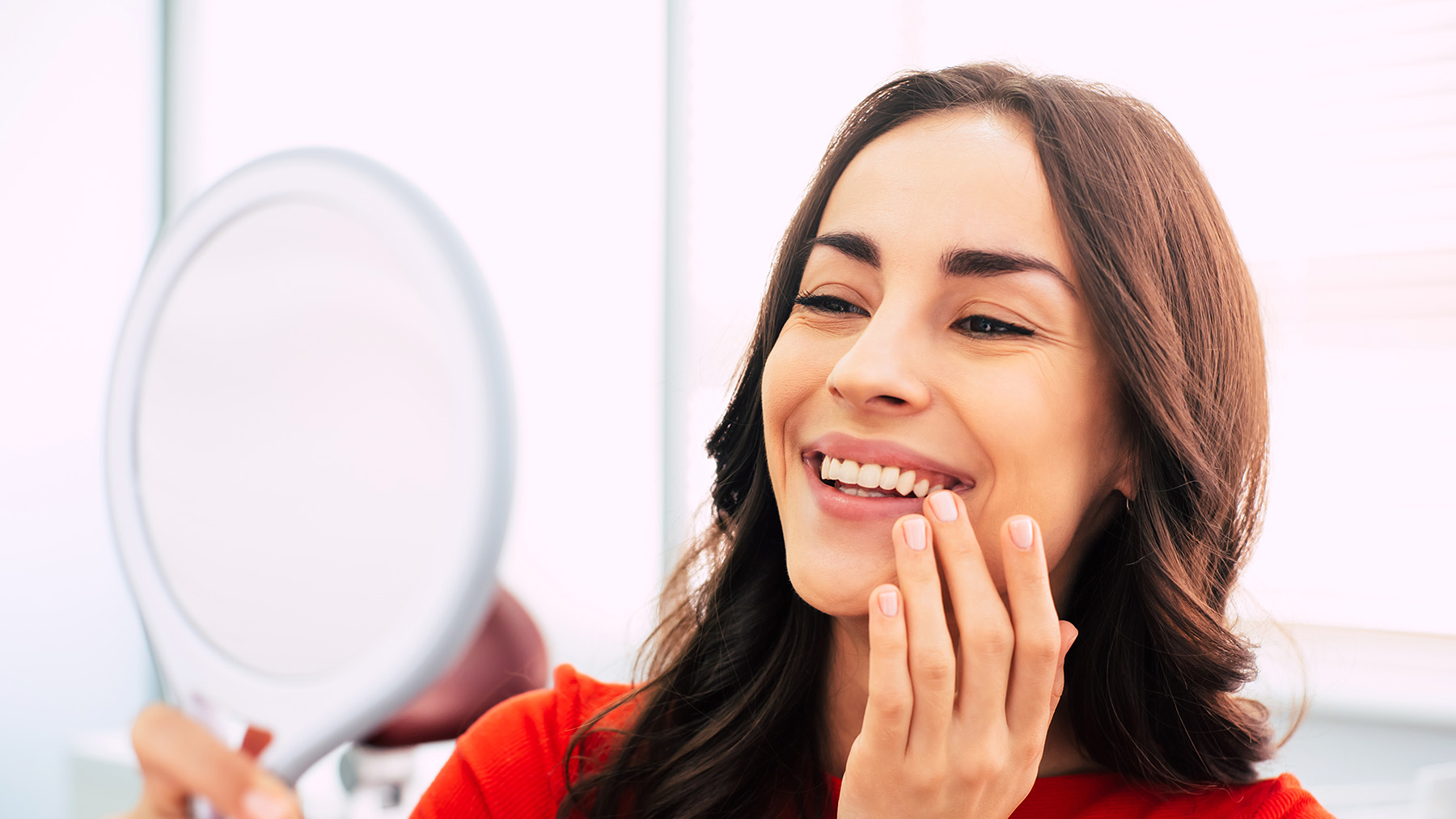 Woman applying makeup at mirror, smiling contentedly.