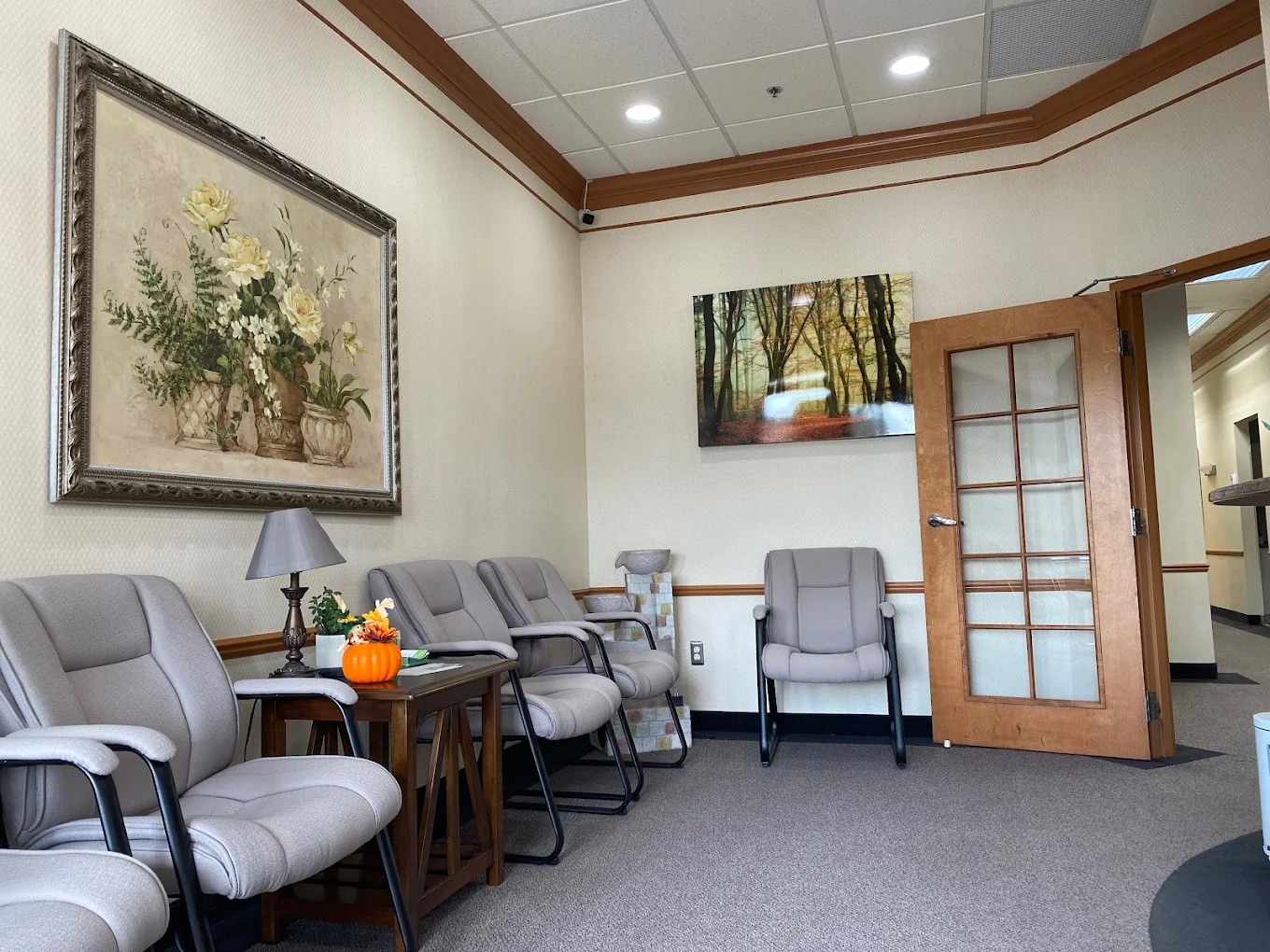 The image shows an interior view of a waiting room with comfortable seating, a framed painting on the wall, and a welcoming atmosphere.