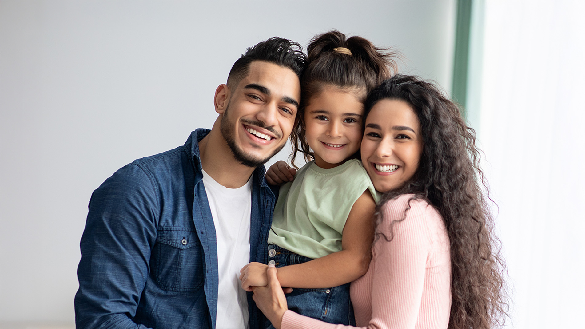 An adult couple posing with their child, all smiling, against a light background.