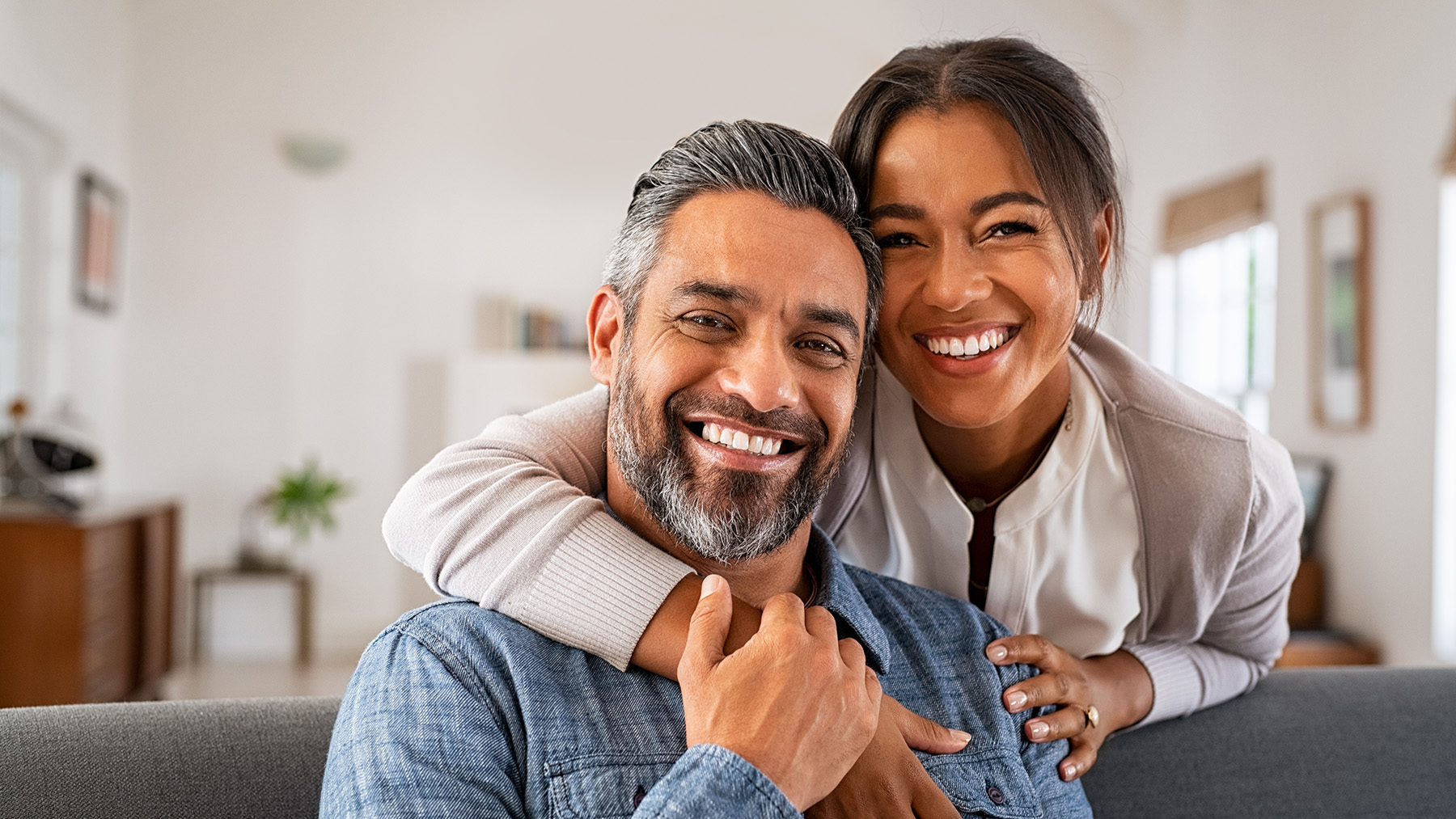 An adult couple sharing a joyful moment while embracing each other, with the man holding his arm around the woman who is smiling broadly.