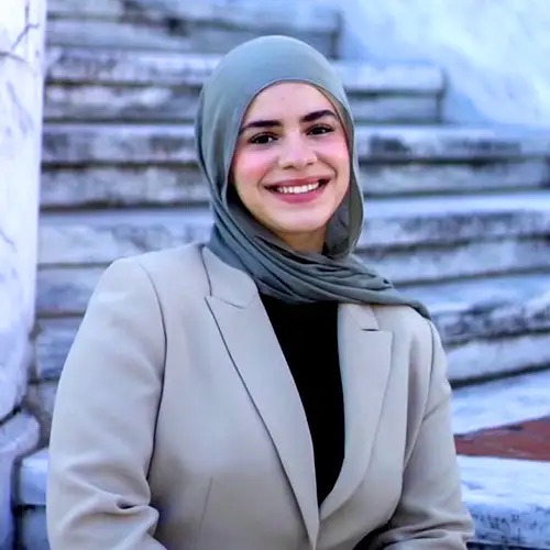 The image shows a person with headscarf smiling at the camera.