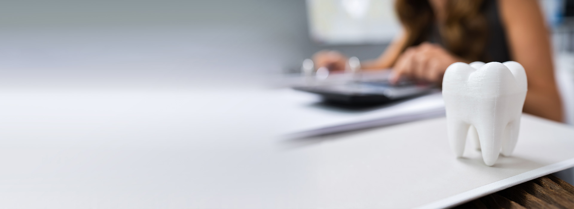 The image shows a person sitting at a desk with a computer monitor, a toothbrush holder with a white toothbrush, and a blurred background of a person working on a document.