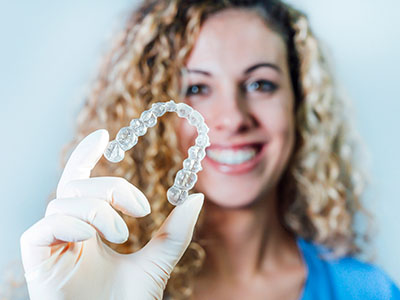 A woman holding up a clear dental retainer with a smile on her face.