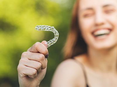 A person holding up a toothbrush with a smiley face on it against a blurred outdoor background.