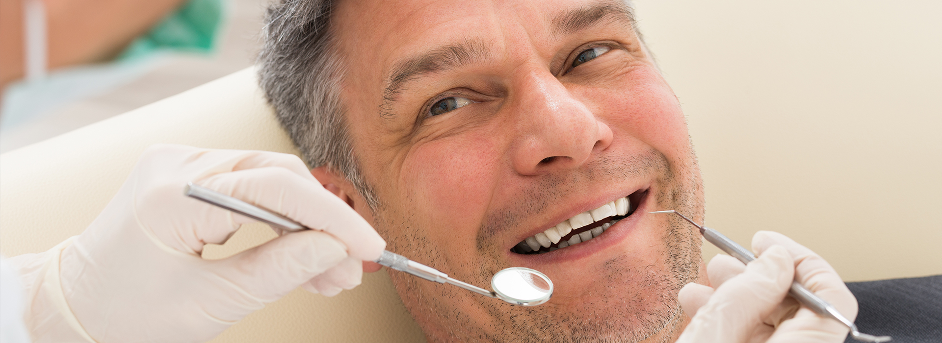 The image shows a man sitting in a dental chair, receiving dental treatment with a dentist working on his teeth.