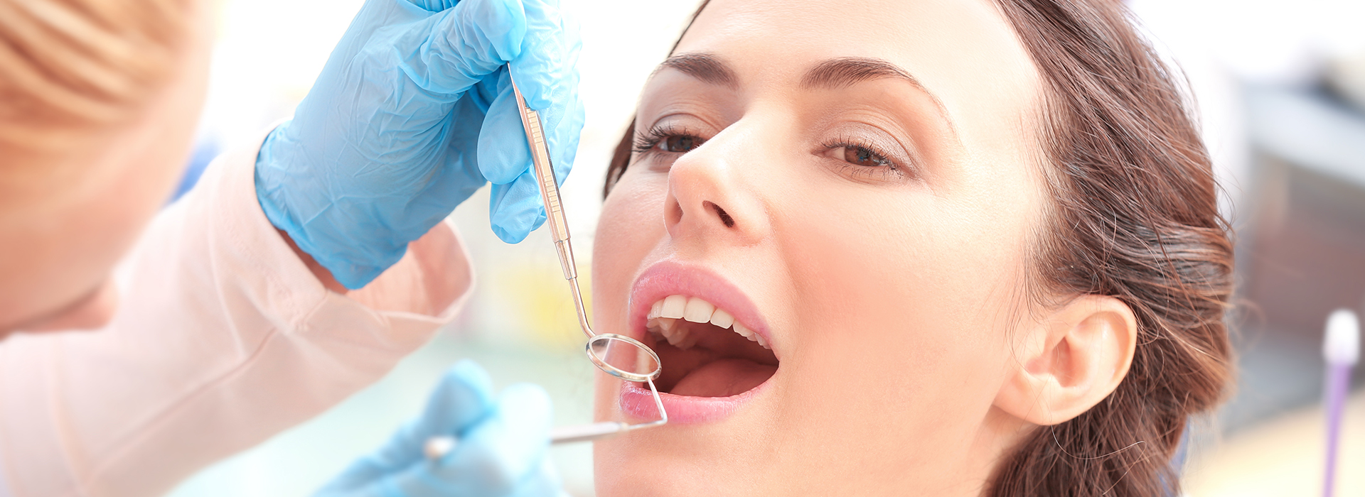 The image shows a woman receiving dental care, with a dentist performing an examination using a magnifying glass, while other dental professionals assist in the background.