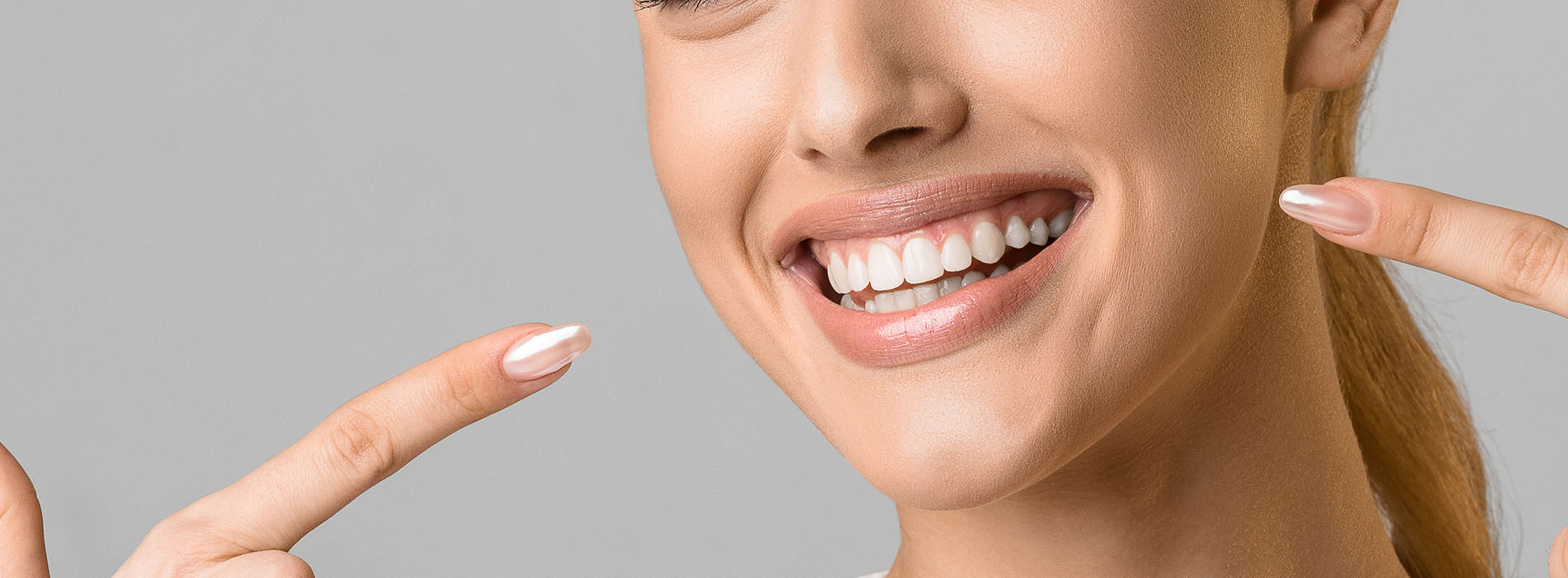 The image features a person with a wide smile pointing at their teeth, which are clearly visible against a white background.