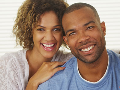A man and woman posing together, smiling and appearing happy, with the man wearing a short beard and the woman with curly hair.