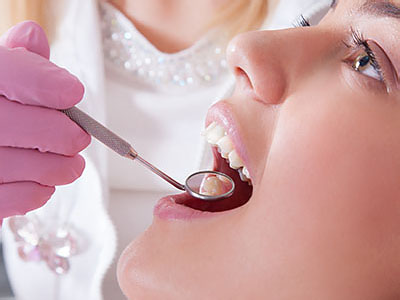 An adult woman receiving dental care with a dentist using tools on her mouth.