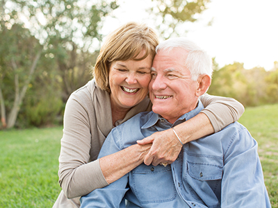 The image shows an older man and woman embracing each other outdoors during daylight hours.