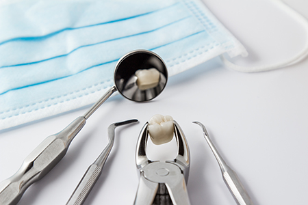 The image displays a collection of dental tools, including scissors, a dental mirror, and a dental pick, with a focus on a toothbrush with a small amount of toothpaste on its bristles, set against a blue surgical mask that covers a white cloth or surface.