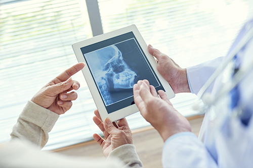 The image shows two individuals holding a tablet displaying an X-ray image, with a medical professional observing the screen while standing behind them.