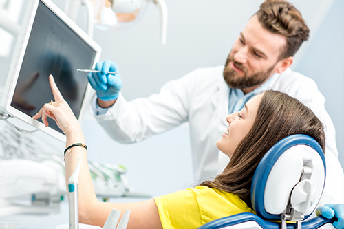 A young woman seated in a dental chair, receiving dental care from a dentist who stands beside her, with both smiling and engaged.