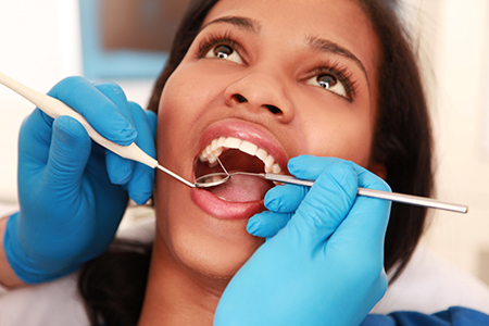 A woman receiving dental treatment with a pair of tweezers held by a dental professional.
