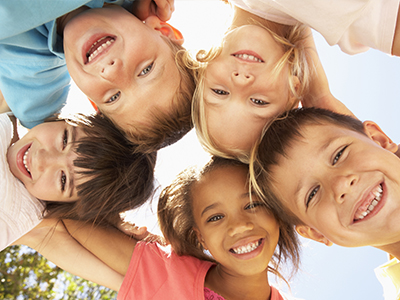 A group of children with smiles on their faces, posing together for a photo, with a sunny sky in the background.
